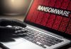 Gloved hand on laptop with ransomware screen.