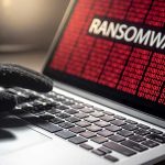 Gloved hand on laptop with ransomware screen.