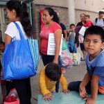 People waiting outside carrying bags boys sitting and playing