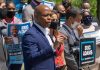 Man speaking at campaign event with supporters behind him