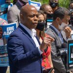 Man speaking at campaign event with supporters behind him