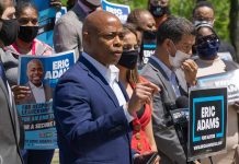 Man speaking at campaign event with supporters behind him