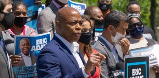 Man speaking at campaign event with supporters behind him