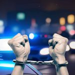 Handcuffed hands raised police cars with lights on