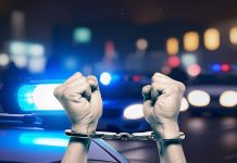 Handcuffed hands raised police cars with lights on