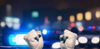 Handcuffed hands raised police cars with lights on