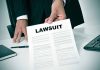 Person holding a document titled "LAWSUIT" in office.