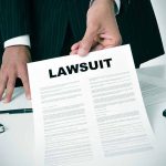 Person holding a document titled "LAWSUIT" in office.