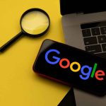 Magnifying glass laptop and smartphone displaying Googles logo