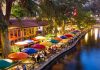 Outdoor riverside restaurant with colorful umbrellas and evening lights
