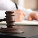 Judges gavel on desk with person writing