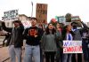 Group of people holding various protest signs outdoors