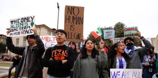 Group of people holding various protest signs outdoors