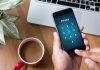 Typing privacy passcode on smartphone near laptop and coffee