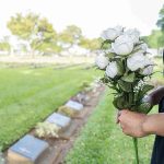 Person holding white roses at a cemetery