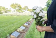 Person holding white roses at a cemetery