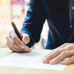 Person signing a document with a pen