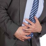 Businessman in a suit holding his stomach appearing to be in discomfort