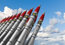 A row of military missiles with red tips and nuclear symbols against a blue sky
