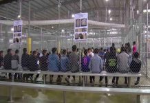 People sitting on benches inside a fenced facility