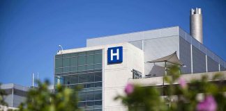 Modern hospital building with a prominent 'H' sign against a clear blue sky