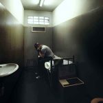 A person sitting in a dimly lit prison cell appearing contemplative and distressed