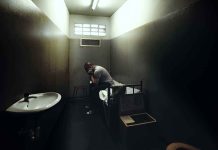 A person sitting in a dimly lit prison cell appearing contemplative and distressed