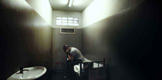 A person sitting in a dimly lit prison cell appearing contemplative and distressed