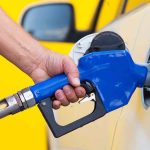 A person refueling a car at a gas station with a blue nozzle