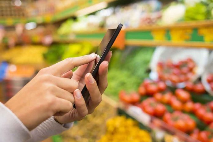 Person using a smartphone while shopping for fresh produce in a grocery store