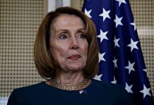 Pelosi Rips Crown: Bold Defiance or Stunt? Person standing near American flag indoors