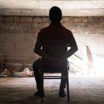 Person tied to chair in dimly lit room