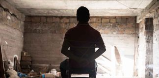 Person tied to chair in dimly lit room