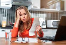Woman looking stressed holding bills in kitchen