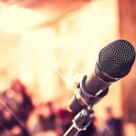 Antifa Professor FLEES to Europe Close up of microphone with blurred audience background