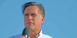 A man speaking into a microphone at an outdoor event against a blue sky