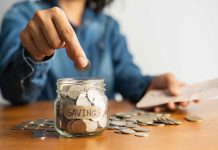 Person placing a coin into a savings jar labeled SAVINGS
