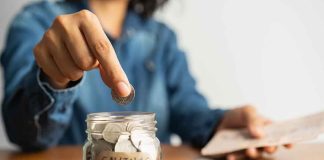 Person placing a coin into a savings jar labeled SAVINGS