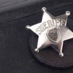 A silver sheriff badge resting on a black leather surface