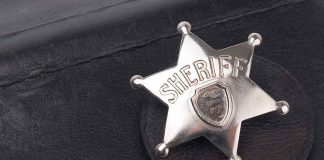 A silver sheriff badge resting on a black leather surface