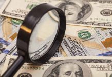 A magnifying glass resting on a pile of US dollar bills