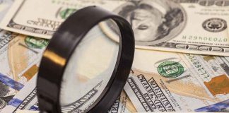 A magnifying glass resting on a pile of US dollar bills