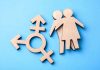 Olympic Controversy: Transgender Ban Looms Wooden transgender symbol and couple figures on blue background.