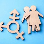 Olympic Controversy: Transgender Ban Looms Wooden transgender symbol and couple figures on blue background.