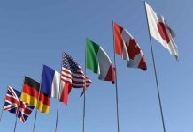 Flags of seven countries against clear blue sky.