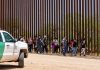 People walking beside tall fence and border patrol vehicle.