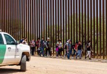 People walking beside tall fence and border patrol vehicle.