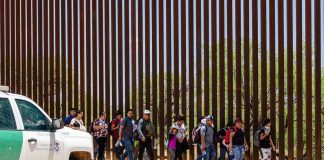 People walking beside tall fence and border patrol vehicle.
