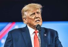 Trump Demands Clinton Probe—Epstein Emails Explode Man in suit speaking at a microphone.