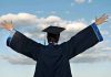 Graduate in cap and gown celebrates under cloudy sky